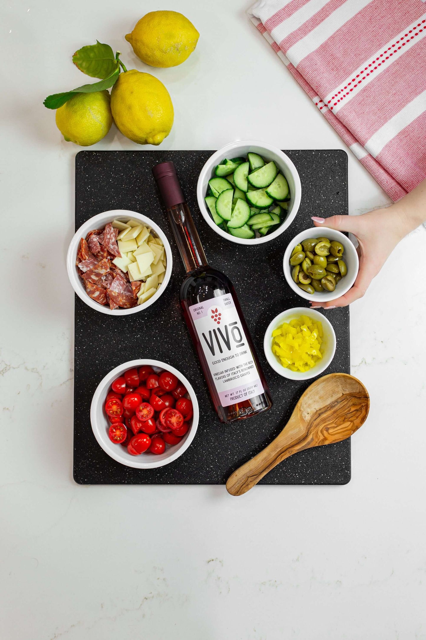 VIVO lambrusco vinegar bottle surrounded by fresh ingredients on a cutting board with lemons.