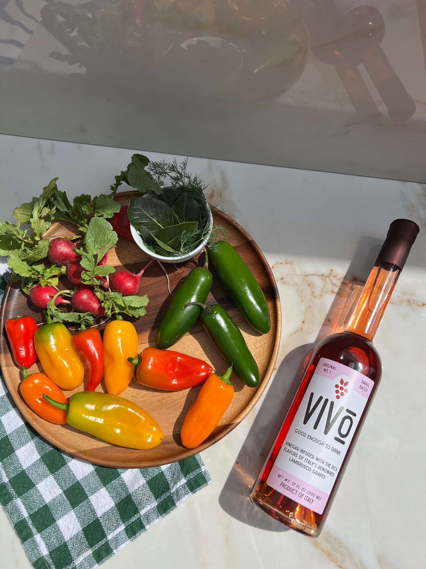 VIVO lambrusco vinegar bottle beside fresh colorful peppers and greens on a wooden plate, showcasing Italian quality.