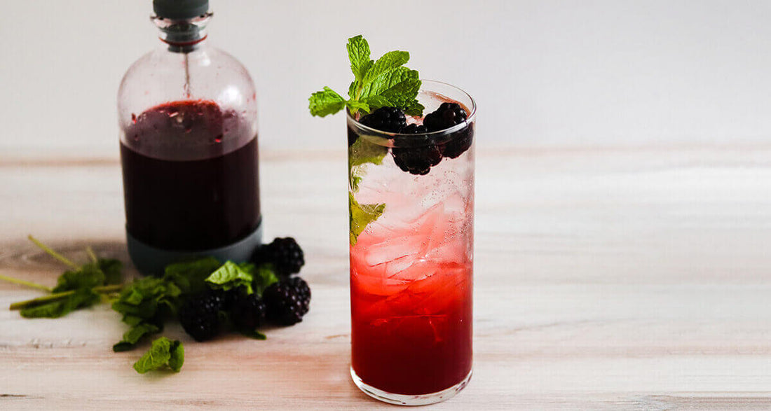 VIVO Lambrusco shrub served over ice with blackberries, mint, and a bottle of vinegar on a marble surface.